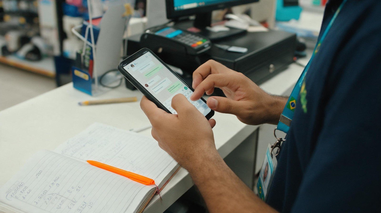 Vendedor respondendo lead no WhatsApp no balcão da loja, com caderno de contas de vendas ao lado